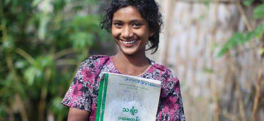Photo of an adolescent girl from Rakhine State/ Myanmar smiling holding a school book